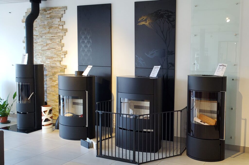 Poêles à bois modernes : showroom et modèles design Exposition de poêles à bois modernes noirs avec barrière de sécurité et panneaux muraux décoratifs en showroom.
